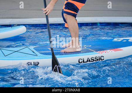 Schwimmen im Pool mit einem Mann auf einem Paddelbrett. Stockfoto