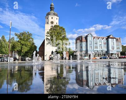 08. Oktober 2023, Brandenburg, Lübben: Die Paul-Gerhardt-Kirche und Wohngebäude auf dem Marktplatz in der brandenburgischen Kreisstadt Lübben spiegeln sich in einem Brunnen wider. Im Landkreis Dahme-Spreewald wird am Sonntag ein neuer Landrat gewählt. Rund 150.000 Bürger sind zur Wahl aufgerufen. Alle über 16 Jahre sind wahlberechtigt. Foto: Patrick Pleul/dpa Stockfoto