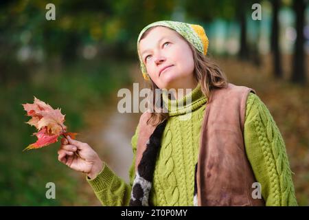Porträt einer Frau in Strickmütze und Pullover mit Herbstlaub. Porträt einer Frau im Alter von 52 Jahren Stockfoto