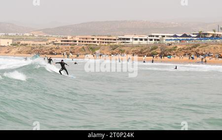 Ein Surfer fängt an einem Februartag in Tamraght in Taghazout Bay in der Nähe von Agadir, Marokko, eine Welle mit Strandhotels im Hintergrund. Stockfoto