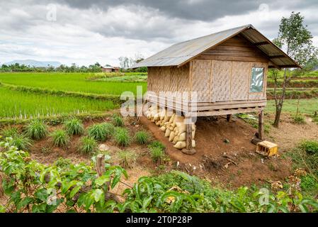 Kleine Holzhütte mit gewelltem Zinndach, darunter liegende Reissäcke, in abgelegener ländlicher Gegend von Bolaven Plateau, Berge in der Ferne, wunderschön, V Stockfoto