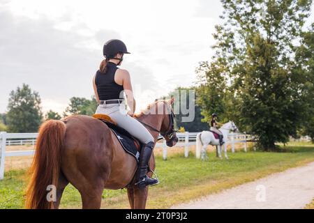 Mädchen in Reitkleidung, die gerne auf dem Weg reiten, lächeln und ihr wunderschönes rotes Pferd streicheln Stockfoto