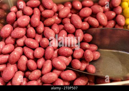 Auf der Theke stehen Süßigkeiten - Erdnüsse in rosafarbener Glasur und ein Löffel. Süßwarenladen. Stockfoto