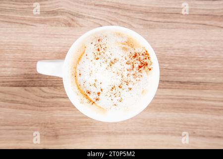 Latte in einem weißen Becher mit Zimt auf einem hölzernen Schneidebrett von oben nach unten Stockfoto