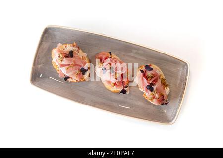 Bruschetta mit Schinken, Kapern und sonnengetrockneten Tomaten auf Ciabatta-Toast isoliert. Hochwertige Fotos Stockfoto
