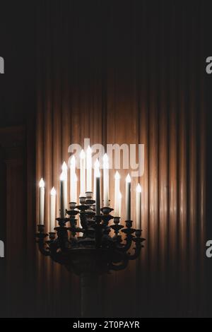 Kerzen, die auf einem kunstvollen und extravaganten Kandelaber brennen, beleuchten einen dunklen Raum mit Holztäfelung und Kopierraum Stockfoto