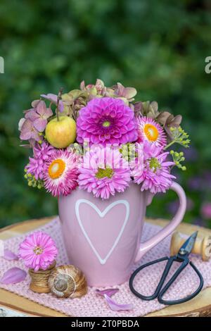 Strauß aus rosa Dahlien, Astern, strohblumen und Hortensien in einer Tasse mit Herzverzierung Stockfoto