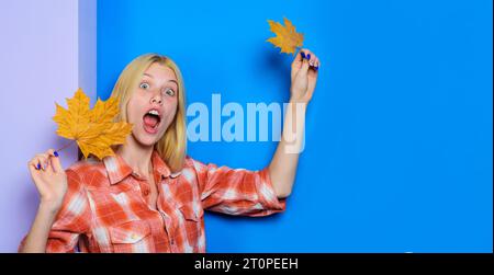 Überraschte Frau in kariertem Hemd mit Herbstlaub. Trendige Herbstmode für Damen. Blondes Mädchen mit gelbem Ahornblatt. Stauntes weibliches Herbstmodell in Stockfoto