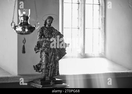 ST.HILARY KIRCHE SONNENLICHT STRÖMT DURCH DAS FENSTER UND BELEUCHTET DIE STATUE VON JESUS Stockfoto