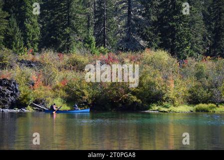 Zwei Männer rudern ein Kanu auf dem Clear Lake in Oregon. Der Herbst hat farbige Büsche entlang der Küste. Farbe wird im Wasser reflektiert. Stockfoto