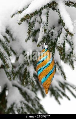 Weihnachtsdekor: Glänzende goldene Kugel auf dem immergrünen Baum. Frostgeschmückte Tannenbäume schaffen ein Winterwunderland. Weihnachtsschmuck: Funkelndes Gold und Blau Stockfoto