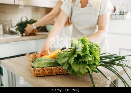 Eine Frau stellt einen Korb mit Zucchini, Salat und Zwiebeln auf den Küchentisch. Diätkost. Stockfoto