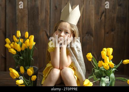 Porträt einer traurigen Prinzessin, die neben gelben Tulpensträußen sitzt. Horizontaler Rahmen. Schaut auf die Kamera. Stockfoto