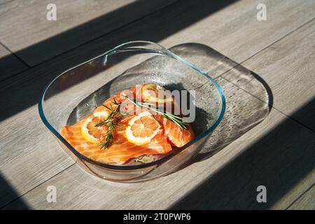 Ein großes saftiges Stück frischer Lachs mit Zitrone und Rosmarin in einer Glasbackform im Ofen Stockfoto