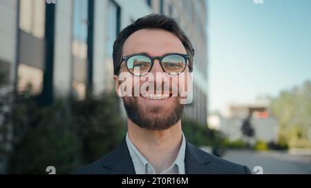 Glücklicher Geschäftsunternehmer erfolgreicher kaukasischer Geschäftsmann in der Nähe des Bürogebäudes vor dem männlichen Porträt lächelnder Kerl in Brillen draußen fröhlicher Mann Stockfoto
