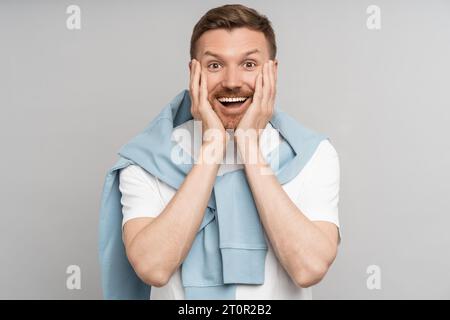 Glücklicher Mann legt überraschend Hände auf die Wangen, fühlt aufrichtiges Glück Freude Freude vereinzelten Hintergrund Stockfoto