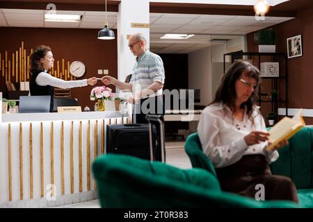 Nach der Anmeldung an der Rezeption in der Hotellobby erhält ein älterer kaukasischer Mann vom Concierge eine Schlüsselkarte. An der luxuriösen Rezeption schließt der alte Reisende den Check-in-Prozess ab. Stockfoto