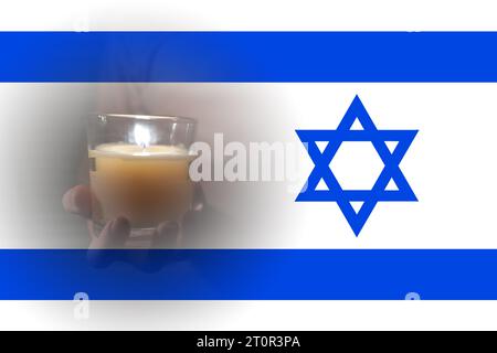 Eine brennende Kerze in den Händen vor dem Hintergrund der israelischen Flagge. Israelisch-palästinensischer Konflikt. Terror der Zivilisten Stockfoto