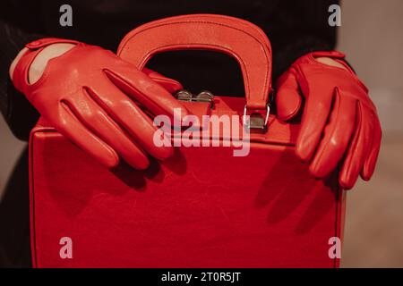 Weibliche Hände in Lederhandschuhen, die eine klassische, hellrote Handtasche halten. Modische Aufnahme Stockfoto