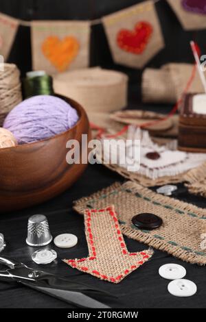 Stücke Sackleinen mit verschiedenen Nähten, Scheren, Fäden, Fingerhut und Knöpfen auf schwarzem Tisch, Nahaufnahme Stockfoto