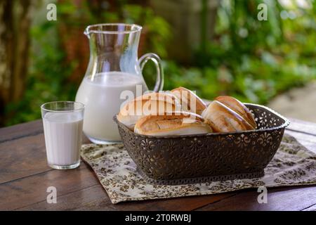 Brot in einem Korb und Milch in einem Glaskrug auf einem Holztisch. Stockfoto