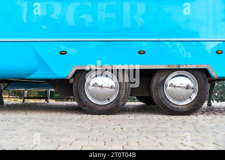 Räder mit glänzenden Scheiben eines großen blauen Food Trucks auf der Stadtstraße. Fahrzeug mit tragbarem Café für Stadtbesucher. Großes Auto mit Fast Food Stockfoto