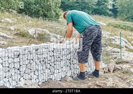 Gelendschik, Russland - 17. August 2021: Wandbau in Gabionen. Builder setzt Steine in ein Metallgitter, um Gabionenwände im Bergpark zu machen Stockfoto