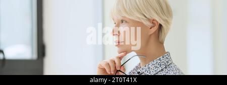 Eine pensive Frau mit kurzen blonden Haaren schaut aus dem Fenster Stockfoto