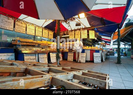 München, Deutschland, EU - 13. September 2023. Frau, die Wein und Käse auf dem Viktualienmarkt kauft, einem berühmten Straßenmarkt in der Altstadt von München. Stockfoto