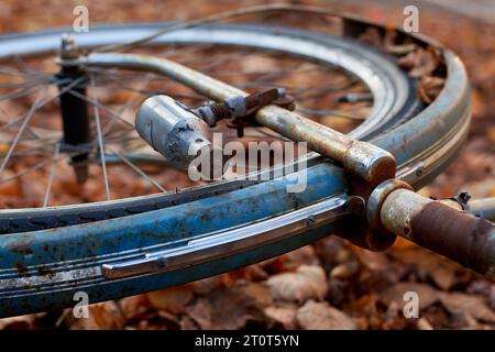 Das Vorderrad eines alten, rostigen Fahrrads, das im Herbst liegt, lässt sich mit dem Dynamo im Fokus Stockfoto