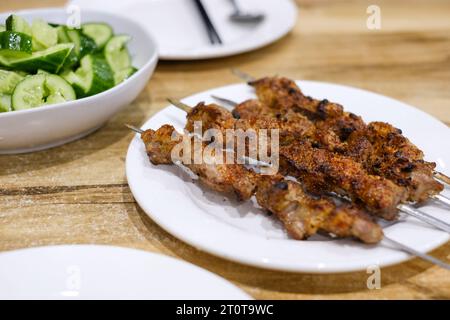 Ein Teller mit Lammspießen und einer Beilage mit Gurkensalat im Appandim Uyghur Restaurant in Burwood - Sydney, NSW, Australien Stockfoto