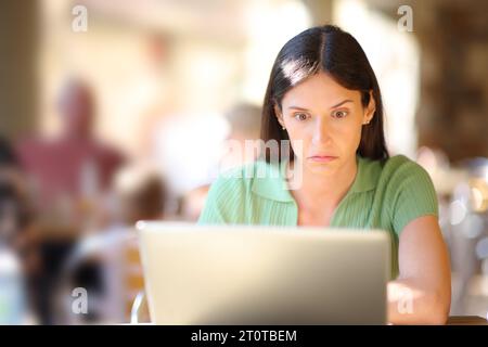 Vorderansicht Porträt einer perplexen Frau, die in einem Restaurant den Laptop überprüft Stockfoto