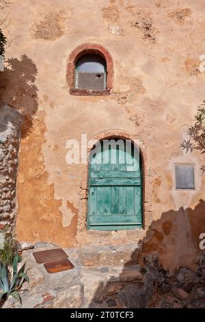 Traditionelles Haus mit ockerfarbenen Wänden und Holztür und -Fenster in der befestigten Stadt Monemvasia, einer Burgstadt der byzantinischen Zeit in Griechenland. Stockfoto