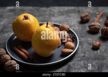 Zwei frische, gelbe Birnen in einer Schüssel mit Nüssen auf dunklem Holzhintergrund Stockfoto