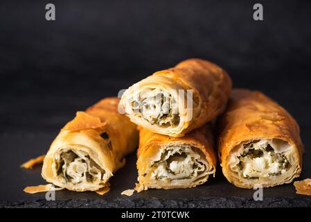 Hausgemachte Brötchen mit Käse und Spinat auf dunklem Hintergrund. Mit goldknuspriger Kruste und köstlicher Füllung Stockfoto