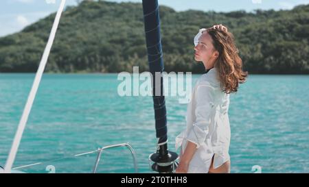 Frau in weißem Hemd entspannt sich beim Stehen auf dem Yachtdeck. Das kaukasische Mädchen genießt eine wunderschöne, meergrüne Insellandschaft. Reise, Tourismus, Urlaub Yachttour zu den Bora Bora Inseln. Zeitlupe 4K Stockfoto