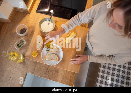 Ernten Sie anonyme Frau, die Olivenöl auf Brottoast setzt, während Sie gesundes veganes Frühstück in der Küche zubereiten Stockfoto