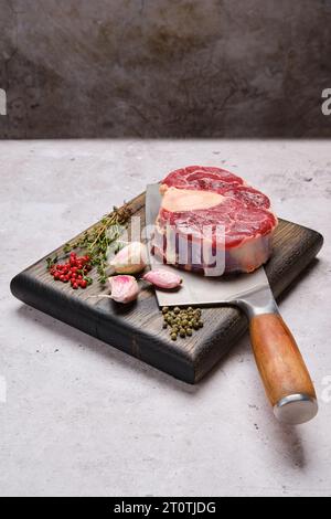 Grosses Stück rohe Rinderhälse, Kreuzschnitt auf dem Spaltbrett mit Gewürz und Kräutern Stockfoto