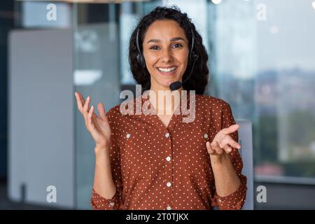 Webkamera-Ansicht, weibliche Mitarbeiterin mit Headset-Telefon spricht Kunden aus der Ferne, Geschäftsfrau, die die Kamera lächelnd ansieht. Stockfoto