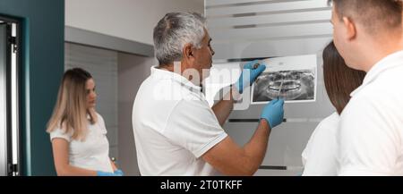 Ein Team von Zahnärzten untersucht Röntgen- und MRT-Aufnahmen von Mundzähnen, diskutiert Behandlungsmethoden und die Machbarkeit der Implantatanwendung in einem Zahnzentrum Stockfoto