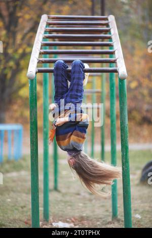 Mädchen mit langen Haaren hängt kopfüber an der horizontalen Stange Stockfoto