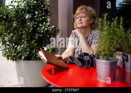 Eine Fotografin sitzt an einem roten Tisch in einem Straßencafé. Stockfoto