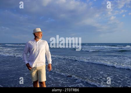 Schöner Mann in weißem Hemd und Hut am Meer Stockfoto