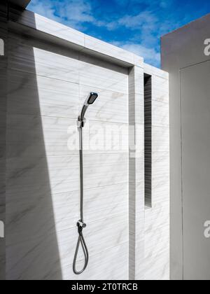 Edelstahl-Außendusche auf Marmorfliesen Wand auf dem Gebäude auf blauem Himmel Hintergrund mit Sonnenlicht und Schatten montiert, minimalistisch, vertikaler Stall Stockfoto