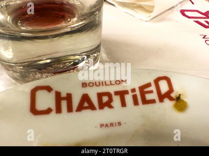 Das Logo auf einem Teller und ein leeres Weinglas nach einer Mahlzeit im historischen Restaurant Bouillon Chartier im Viertel Grands Boulevards von Paris, Fra Stockfoto