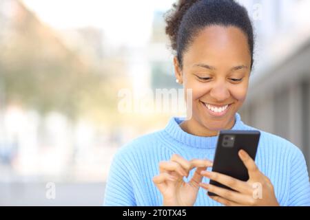 Vorderansicht einer glücklichen Frau, die ein Smartphone benutzt und auf der Straße lächelt Stockfoto