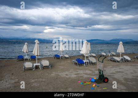 Kalamaki, Korfu, Griechenland - Sonnenliegen und Sonnenschirme am Kalamaki Strand im Nordosten der griechischen Insel Korfu. Im Hinterland Albanien mit den s Stockfoto