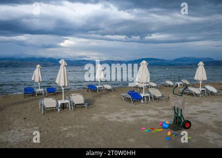 Kalamaki, Korfu, Griechenland - Sonnenliegen und Sonnenschirme am Kalamaki Strand im Nordosten der griechischen Insel Korfu. Im Hinterland Albanien mit den s Stockfoto