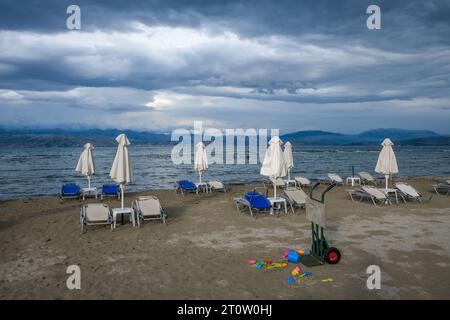 Kalamaki, Korfu, Griechenland - Sonnenliegen und Sonnenschirme am Kalamaki Strand im Nordosten der griechischen Insel Korfu. Im Hinterland Albanien mit den s Stockfoto