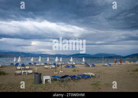 Kalamaki, Korfu, Griechenland - Sonnenliegen und Sonnenschirme am Kalamaki Strand im Nordosten der griechischen Insel Korfu. Im Hinterland Albanien mit den s Stockfoto